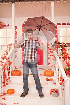 Teenager in fall. Portrait of a nice teen boy walking near the house with an umbrella on a warm autumn day. child have