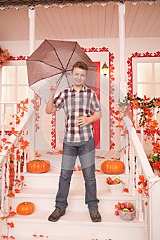 Teenager in fall. Portrait of a nice teen boy walking near the house with an umbrella on a warm autumn day. child have