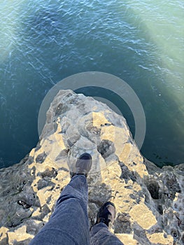 Teenager feet in sneakers stand on a cliff by the sea. Sea view from above. Deep sea