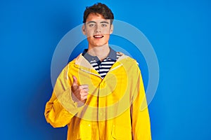 Teenager fisherman boy wearing yellow raincoat over isolated background doing happy thumbs up gesture with hand