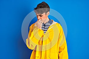 Teenager fisherman boy wearing yellow raincoat over isolated background looking stressed and nervous with hands on mouth biting