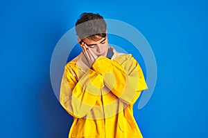 Teenager fisherman boy wearing yellow raincoat over isolated background sleeping tired dreaming and posing with hands together