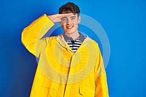 Teenager fisherman boy wearing yellow raincoat over isolated background very happy and smiling looking far away with hand over