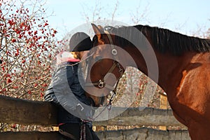 Teenager girl and bay horse hugging each other