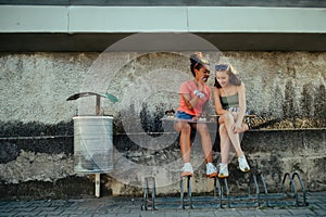 Teenager girl best friends with skateboards spending time outdoors in city during warm summer holiday day. Sitting on