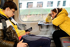 Teenager girl and boy with headphones on her head sitting in a suburban train