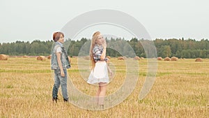 Teenager girl and boy walking on harvesting field on haystack background. Happy girl and boy having fun on countryside