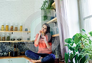 A teenager girl in a bright kitchen drinks red cherry and apple juice in a glass. Modern lifestyle. Healthy food, fresh