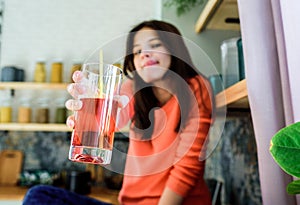 A teenager girl in a bright kitchen drinks red cherry and apple juice in a glass. Modern lifestyle. Healthy food, fresh fruits at