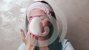 A teenager girl cleans her face with a foam pink sponge, clean skin, cosmetology. Daily morning facial cleansing
