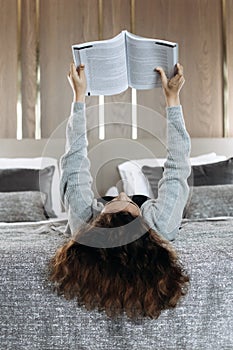 Teenager girl with curly hair lying on bed and reading book