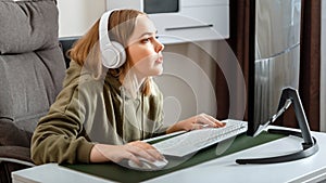 Teenager girl cybersportman gamer play online computer game at home alone in leisure time. Young blonde woman in headphones