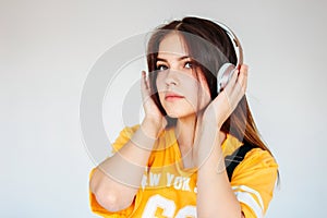 Teenager girl with dark long hair in yellow t-shirt listening music or podcast in headphones isolated on grey background