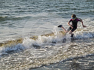 Teenager girl in dark wet suit and shoes jumping in the ocean, West coast of Ireland, Atlantic ocean. Outdoor activity concept