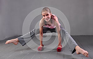 Teenager girl doing exercises with dumbbells to develop with dumbbells muscles on grey background. Full length portrait of teen ch
