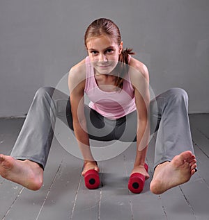 Teenager girl doing exercises with dumbbells to develop with dumbbells muscles on grey background. Full length portrait of teen ch