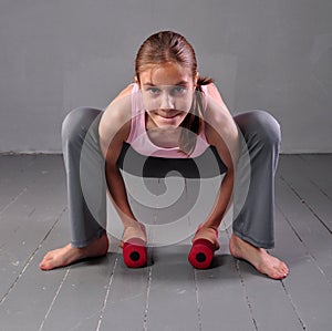 Teenager girl doing exercises with dumbbells to develop with dumbbells muscles on grey background. Full length portrait of teen ch