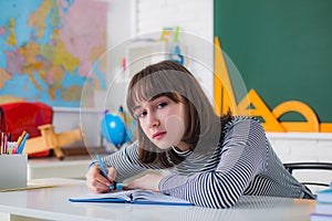 Teenager girl drawing picture in class. Close up face. Teenager is learning in class on background of blackboard