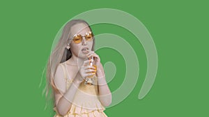 Teenager girl drinking orange juice by straw from glass on transparent green background. Young girl enjoying fresh