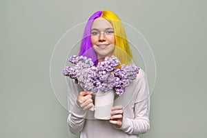 Teenager girl with dyed purple yellow hair holding lilac flowers in hands