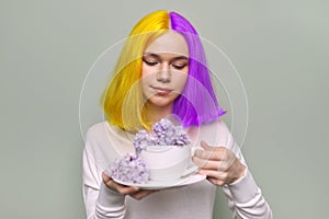 Teenager girl with dyed purple yellow hair holding lilac flowers in hands