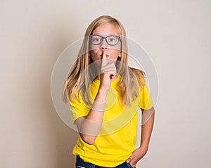 Teenager girl in eyeglasses putting finger up to lips and ask si