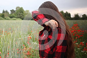 Teenager girl in a field with blooming red poppies crying, wiping tears with her shirt sleeve, concept of unhappiness,