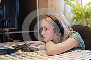 Teenager girl in green clothes with black headphones for remote learning via a computer from home room. Distance learning online