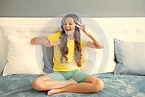 Teenager girl in headphones relax on bed at home using headphones, singing. Happy teen girl, positive and smiling