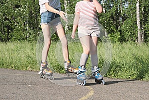 teenager girl and her little sister rollerskating in the park. partial view. sport and leisure concept. preshcool girl