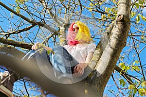 Teenager girl, hipster sitting high on a tree. Spring, nature sky background