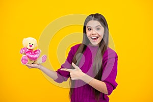 Teenager girl hold soft toy for birthday on yellow background. Teen with toy teddy bear with love heart for valentines