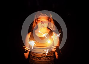 Teenager girl holding a burning sparklers in her hands.