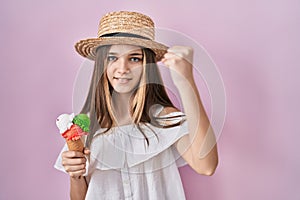 Teenager girl holding ice cream angry and mad raising fist frustrated and furious while shouting with anger