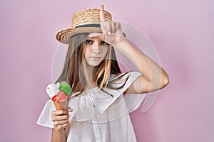 Teenager girl holding ice cream making fun of people with fingers on forehead doing loser gesture mocking and insulting