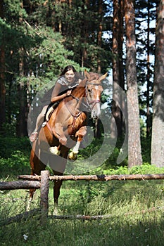 Teenager girl jumping over the fence with horse