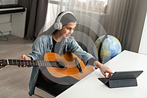 Teenager girl learning to play guitar at home using online lessons. Hobby remote musical education acoustic guitar. Copy