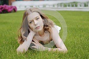 A teenager girl lies on the grass in a beautiful white dress, rests, enjoys nature. Girl with short blond hair. Beautiful and