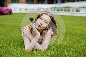 A teenager girl lies on the grass in a beautiful white dress, rests, enjoys nature. Girl with short blond hair. Beautiful and