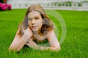 A teenager girl lies on the grass in a beautiful white dress, rests, enjoys nature. Girl with short blond hair. Beautiful and