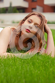 A teenager girl lies on the grass in a beautiful white dress, rests, enjoys nature. Girl with short blond hair. Beautiful and