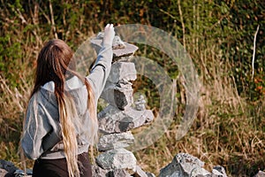 Teenager girl with long hair finishing building very complicated balance stone tower. Selective focus. Patience and internal zen