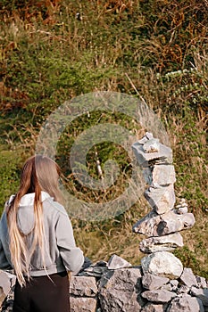 Teenager girl with long hair finishing building very complicated balance stone tower. Selective focus. Patience and internal zen