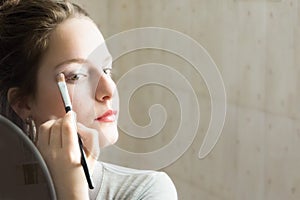 Teenager girl looking her self in a mirror applying eyeshadow wi