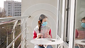 Teenager girl in mask and headphones, listening to music on smartphone, on open balcony. spring sunny day. quarantine