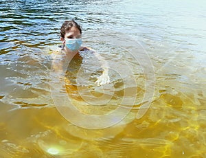 A teenager girl in a medical protective mask swims in the river.