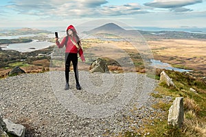 Teenager girl model taking selfie on a hike in a mountains, beautiful scenery in the background. Letterfrack, Connemara National