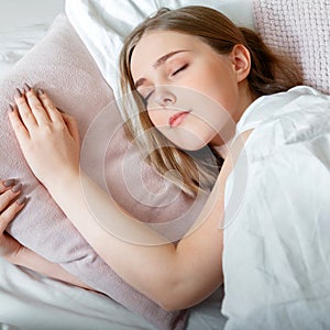 Teenager girl in pajamas sleeps in bedroom at morning time. Young Woman sleeping in bed. Portrait of blonde teen girl