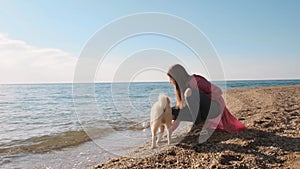 Teenager girl in a pink coat tryies the water in the sea with her siba inu white dog slow motion