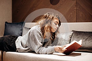 Teenager girl reading book on the couch at home